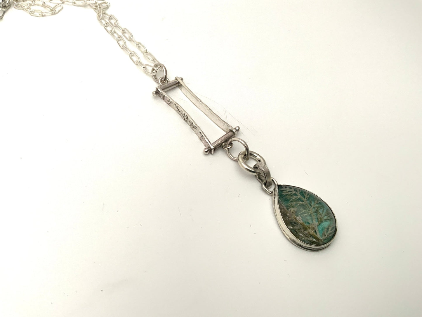 Botanical pendant with yarrow and tiny flowers preserved in resin over watercolor background